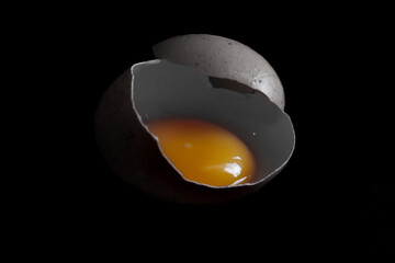 close up of an egg yolk inside the shell, egg yolk isolated on black background