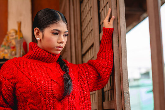 A contemplative young Filipino woman in a red sweater visits a serene South Korean temple, reflecting on the culture.
