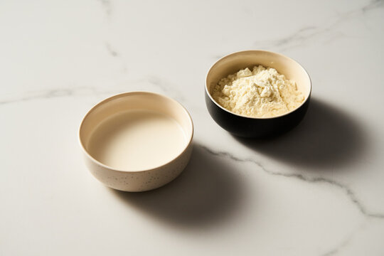 Dry powdered milk and usual milk in the bowl on white marble background, Minimalistic food photo.