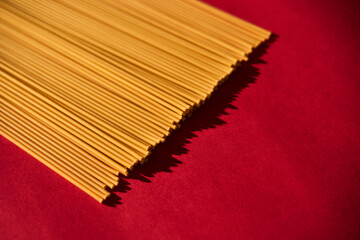 Bucatini raw pasta macaroni background on vibrant and contrast red backgrorund. Hard light,...