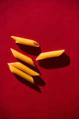 Penne raw pasta macaroni background on vibrant and contrast red backgrorund. Hard light, contrast...
