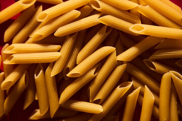 Penne raw pasta macaroni background on vibrant and contrast red backgrorund. Hard light, contrast...