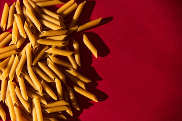Penne raw pasta macaroni background on vibrant and contrast red backgrorund. Hard light, contrast...
