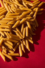 Penne raw pasta macaroni background on vibrant and contrast red backgrorund. Hard light, contrast...