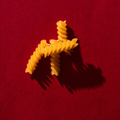 Fusilli raw pasta macaroni background on vibrant and contrast red backgrorund. Hard light, contrast...
