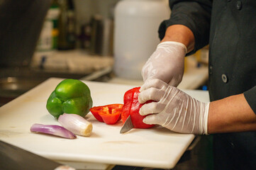 Chef's gloved hands chopping red and green bell peppers