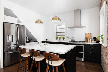 A beautiful farmhouse detail kitchen with black cabinets and island, gold lights and faucet, and stainless steel appliances. No brands or labels.