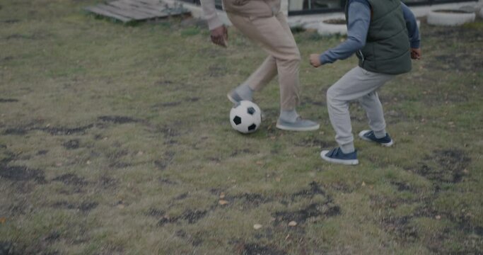 Slow motion of dad and son playing soccer game on lawn running kicking ball having fun together. Sports and family activity concept.