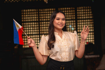 Portrait of a young tour guide holding a Philippine flag, dressed in elegant traditional Filipino...