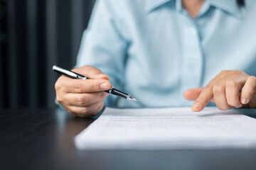 Woman signing document, focus on female hand holding pen, putting signature at official paper. Close up businesswoman signing documents. Hand of woman write business document charts at office desk.