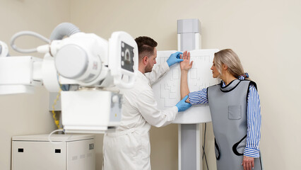 A specialist doctor in an X-ray room, a radiologist sets up a machine for radiography of a patient...