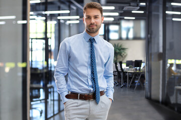 Handsome young businessman standing in modern office with collegues on the background.