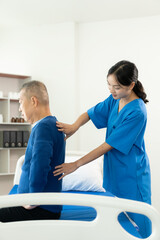 An old Asian man is doing physical therapy with the support of a nurse in the living room by...