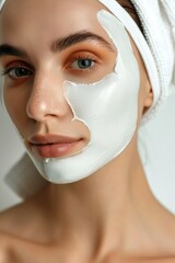 A woman with a white face mask on her face. She has a white towel wrapped around her head