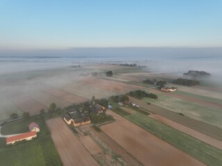Brzask na wsi z lotu ptaka, ujęcia z drona wsi o brzasku, wschód słońca na wsi, pusząca się o poranku wieś, pola owite mgłą o brzasku, poranek we mgle © klumb