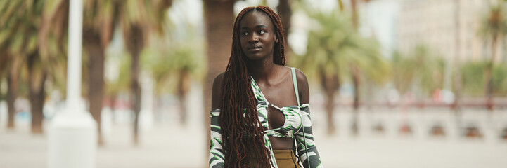 Gorgeous woman with African braids wearing walks down the street. Stylish girl walking on the park,...