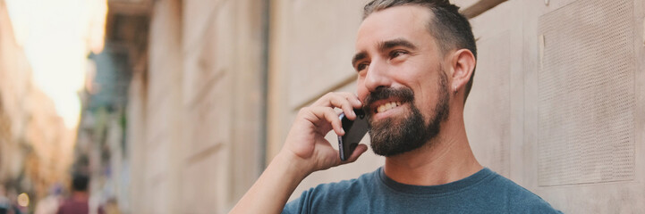 Close-up of young man with beard talking on cellphone against the background of the old city, Panorama