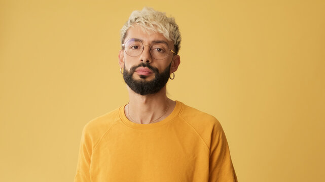 Guy with glasses, dressed in yellow T-shirt looking at camera, isolated on yellow background in studio