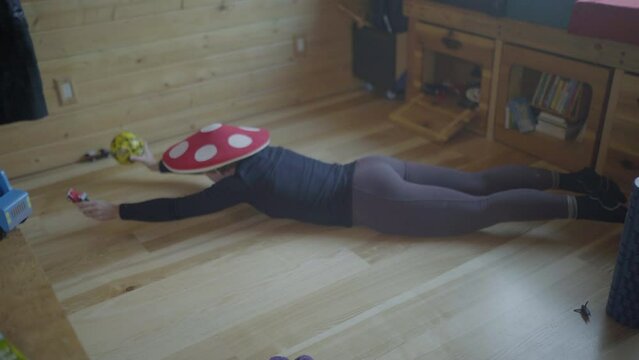Lockdown Shot Of Woman Wearing Mushroom Cap Lying On Floor While Balancing Over Stomach At Home - Fairbanks, Alaska