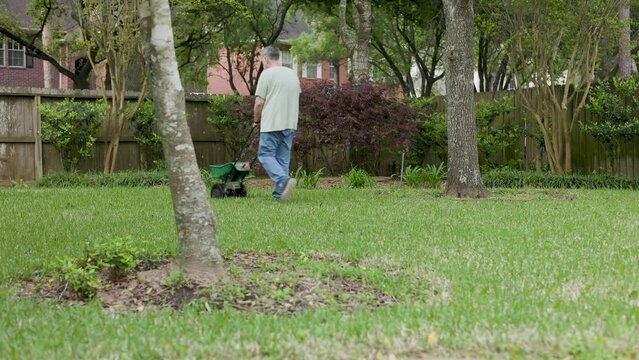 elderly man using a spreader to fertilize his yard