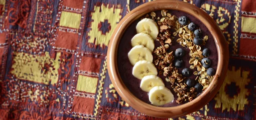 Poster overhead view of acai berry smoothie bowl with fruit toppings on colorful ethnic textile © Klay
