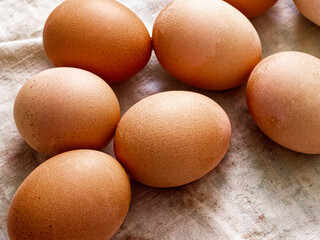 A close-up shot of 6 speckled brown eggs lying on a wrinkled cloth, giving off a rustic and homely vibe.