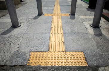 Yellow tactile paving for blind people or visually impaired on the sidewalk