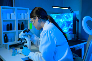 A woman in a lab coat is looking through a microscope