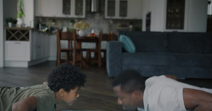 Joyful African American family father and son doing push-ups training together and doing high-five hand gesture at home. People and active lifestyle concept.