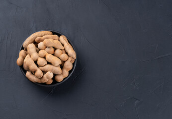 Tamarind fruit in shell and bowl on empty dark background, top view. Copy space
