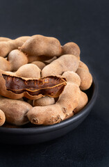 Part of a bowl filled with tamarind fruit in the shell close-up