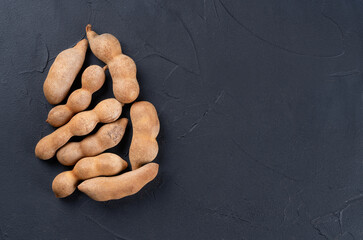 Pile of tamarind fruits on empty dark background, top view. Copy space