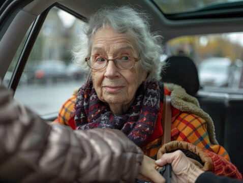 Una signora anziana scende dall'auto, l'assistente la aiuta, tenendole le mani. Una donna anziana ha difficolt&agrave; ad alzarsi dal sedile posteriore dell'auto