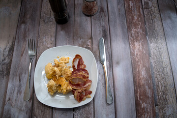 scrambled eggs with bacon on a plate. on the table are a salt mill and a pepper mill for seasoning. view from above