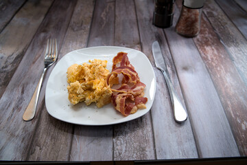 scrambled eggs with bacon on a plate. on the table are a salt mill and a pepper mill for seasoning....