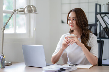 A young woman takes a thoughtful pause with a cup of coffee during a busy workday at home office.