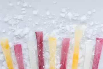 A row of DIY fruit flavoured freezies with ice pieces scattered around.