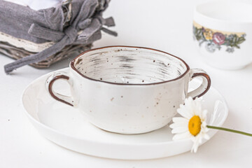 A wicker basket, a ceramic soup bowl, white chamomile flower on white background. Summer home atmosphere, kitchen dishware, product display or design key visual layout.