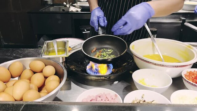 The Professional Hotel chef is cooking by putting various ingredients into frying pan in interior of modern restaurant kitchen.