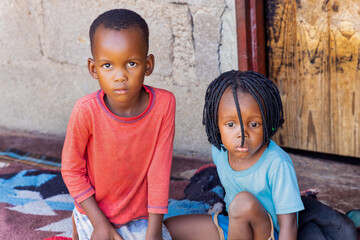 village two african kids playing on the porch in front of the house, sitting on a blanket