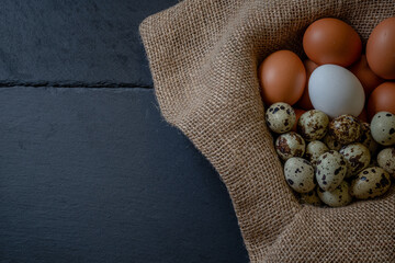 Fresh chicken and quail eggs in a basket on a sack, wooden table.Selective focus