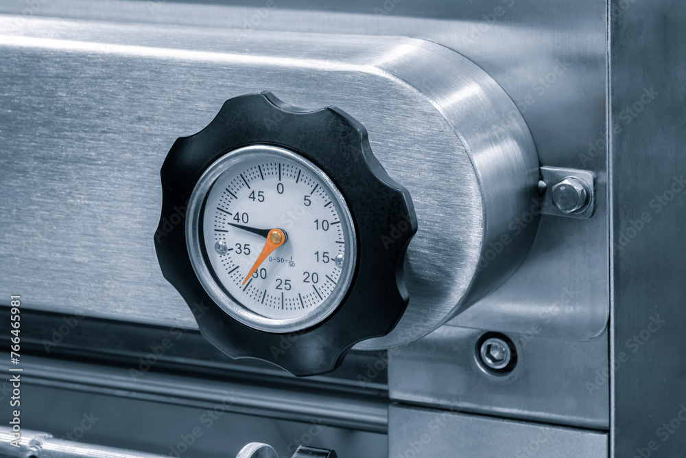 Poster A small black and silver device with a red number 12 on it. The device is attached to a wall. Pressure gauge, thermometer or other measuring instrument on an industrial machine or conveyor