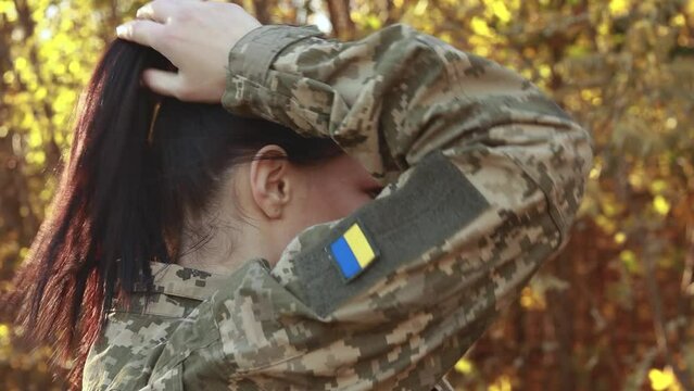 Female servicewoman brave soldier dressed in the camouflage military uniform, fixes her hair, symbol of independence. Armed Forces of Ukraine. Woman serving in ukrainian army troops
