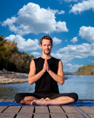 A caucasian man sitting on the pier by the river and doing yoga outdoor - 766470927