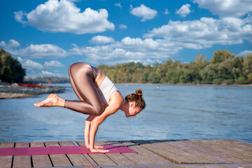 Full length of a female yoga coach practicing yoga on the pier by the river - 766470931