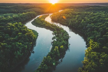 The sun sets over a serene river winding through a forested landscape - obrazy, fototapety, plakaty