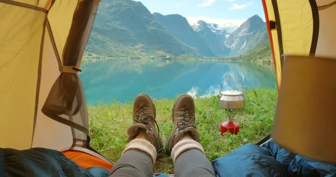 Feet, camping tent and relaxing on vacation, travel and mountain view on morning in nature. Person, drinking coffee and lazy on holiday, hot beverage and tea on outdoor adventure at lake or river pov