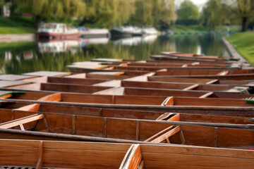 Row of empty Punts moored on the River Cam at Cambridge with defocused boats in the background