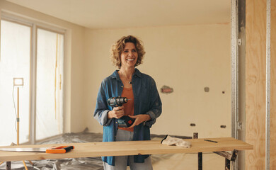Woman holding a drill gun while renovating her home's kitchen - 766486173