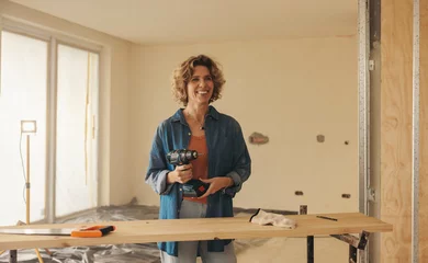 Wandaufkleber Woman holding a drill gun while renovating her home's kitchen © Jacob Lund
